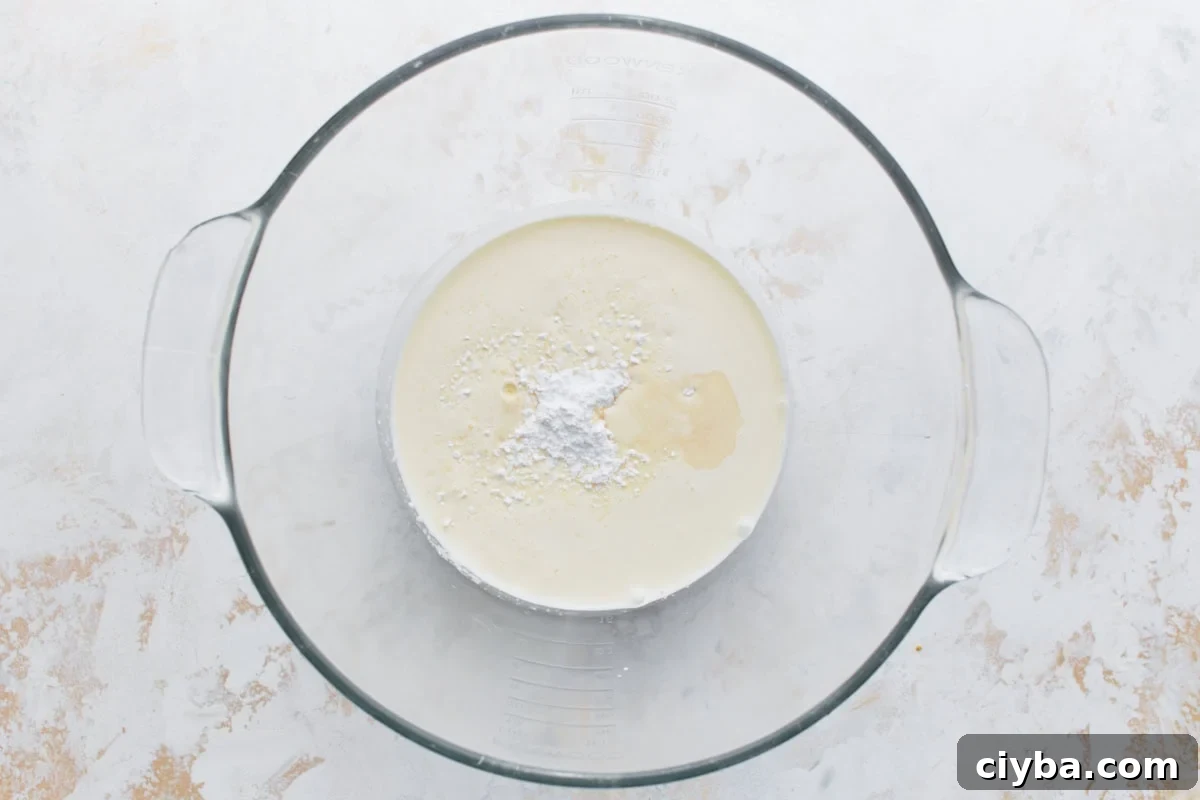 Whipped cream ingredients—heavy cream, powdered sugar, and vanilla—added to a glass mixing bowl before whipping.