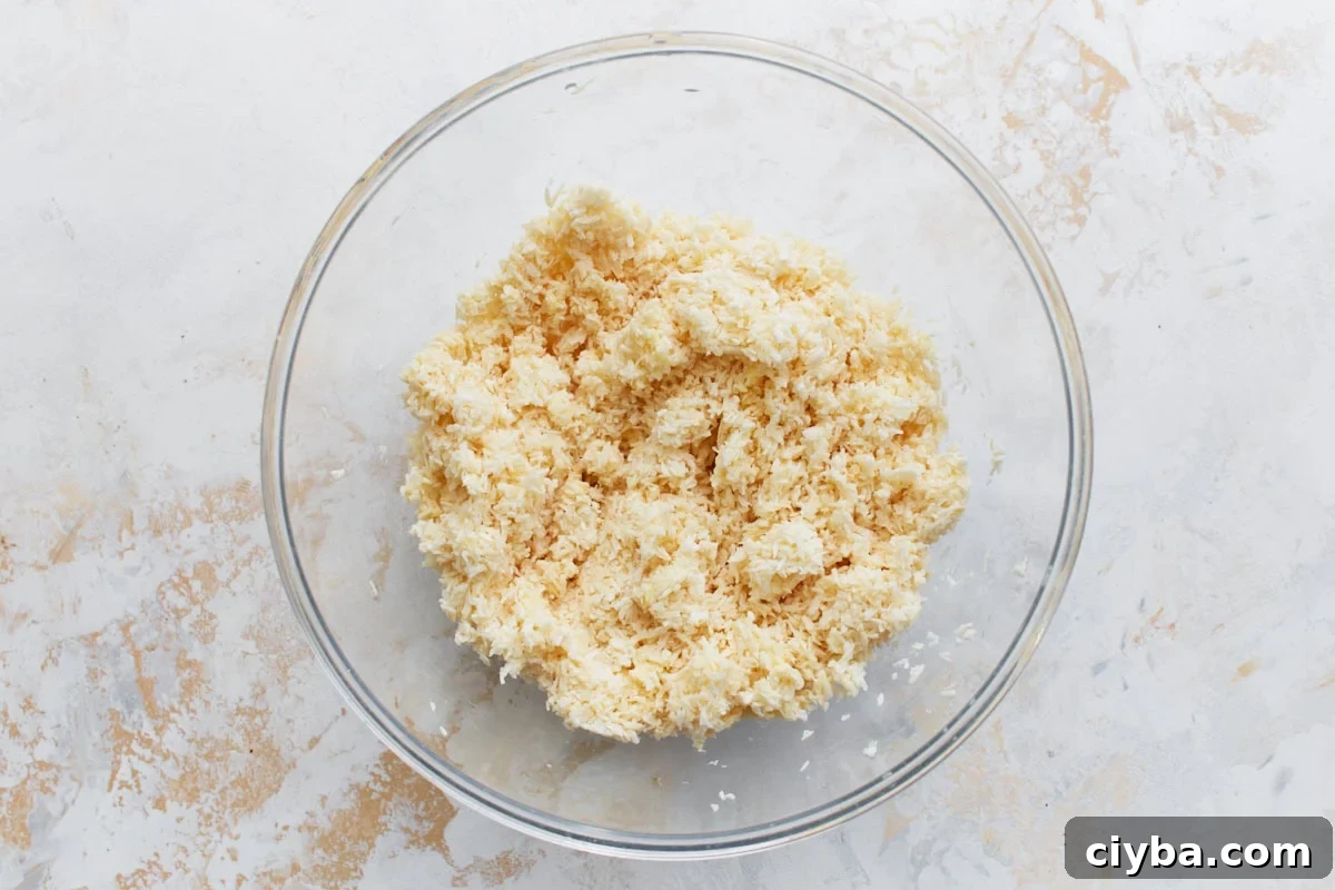 Large mixing bowl filled with shredded sweetened coconut, egg whites, and melted butter for the crust mixture.