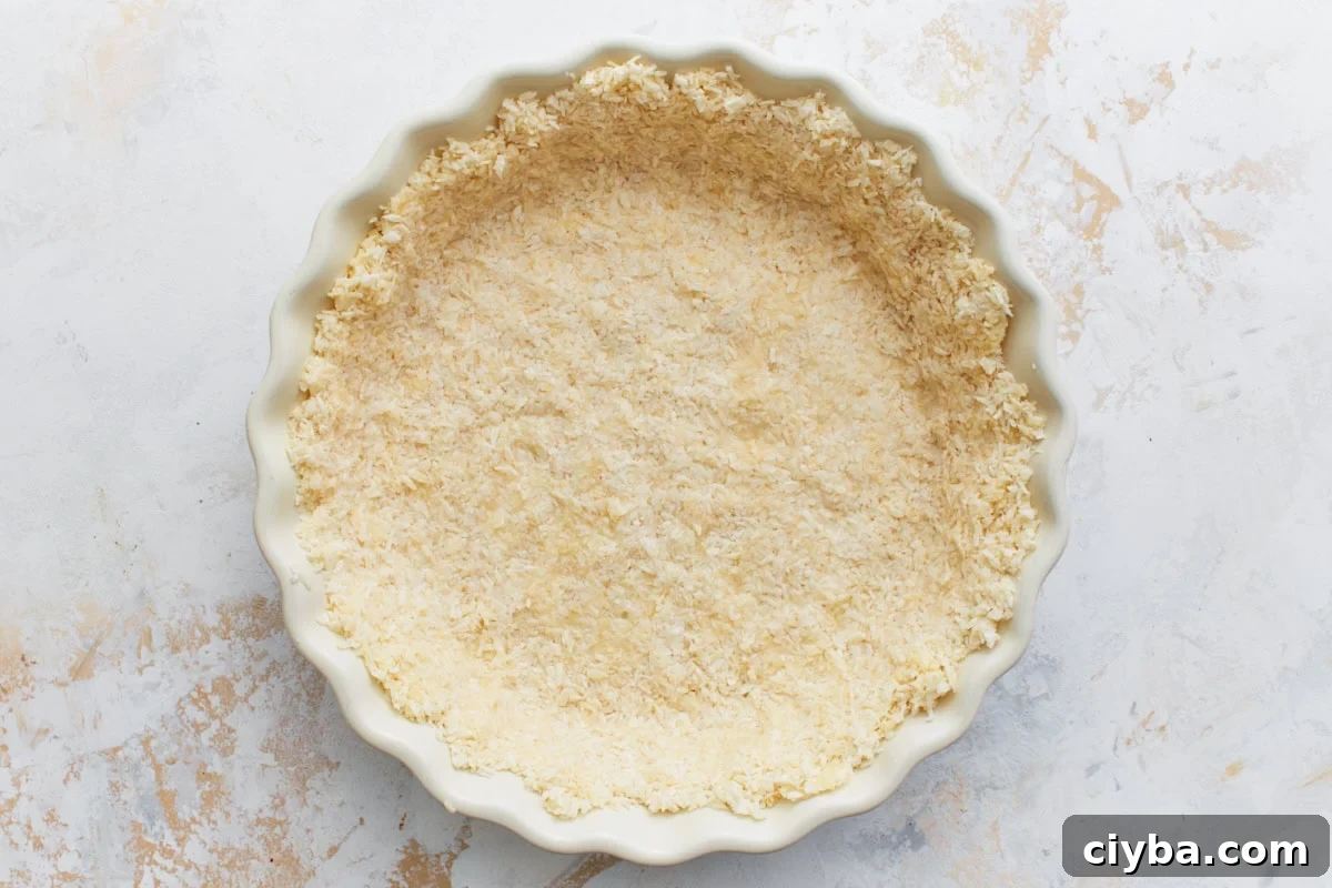 Unbaked coconut crust mixture pressed evenly into a fluted pie dish.