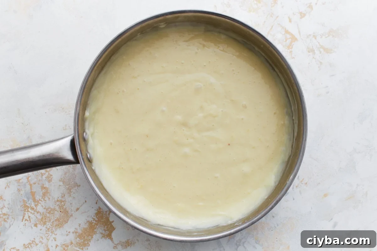 Custard mixture in a saucepan beginning to thicken as it cooks.