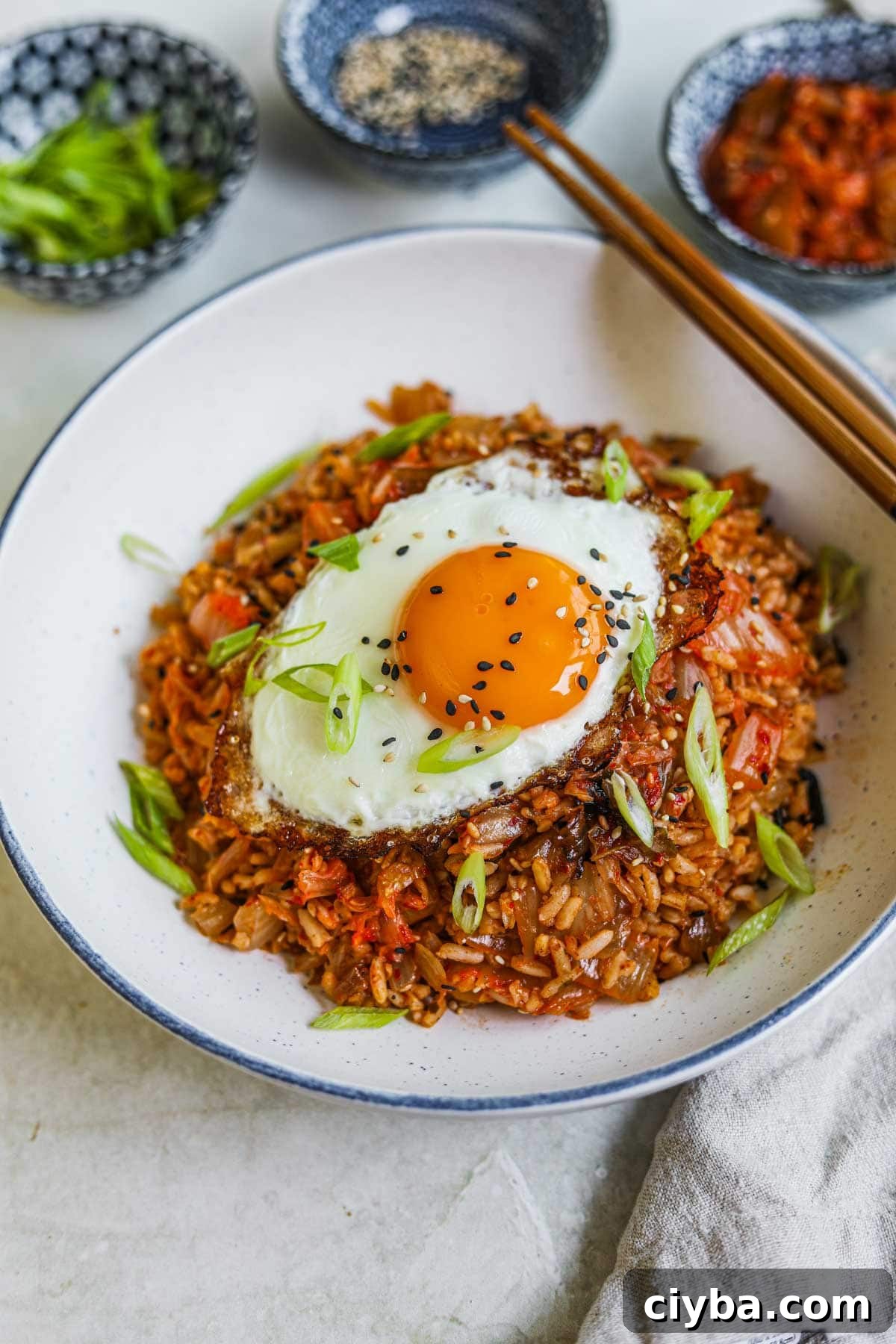 Easy kimchi fried rice in a bowl with a fried egg, sesame seeds, and scallions on top with chopsticks.