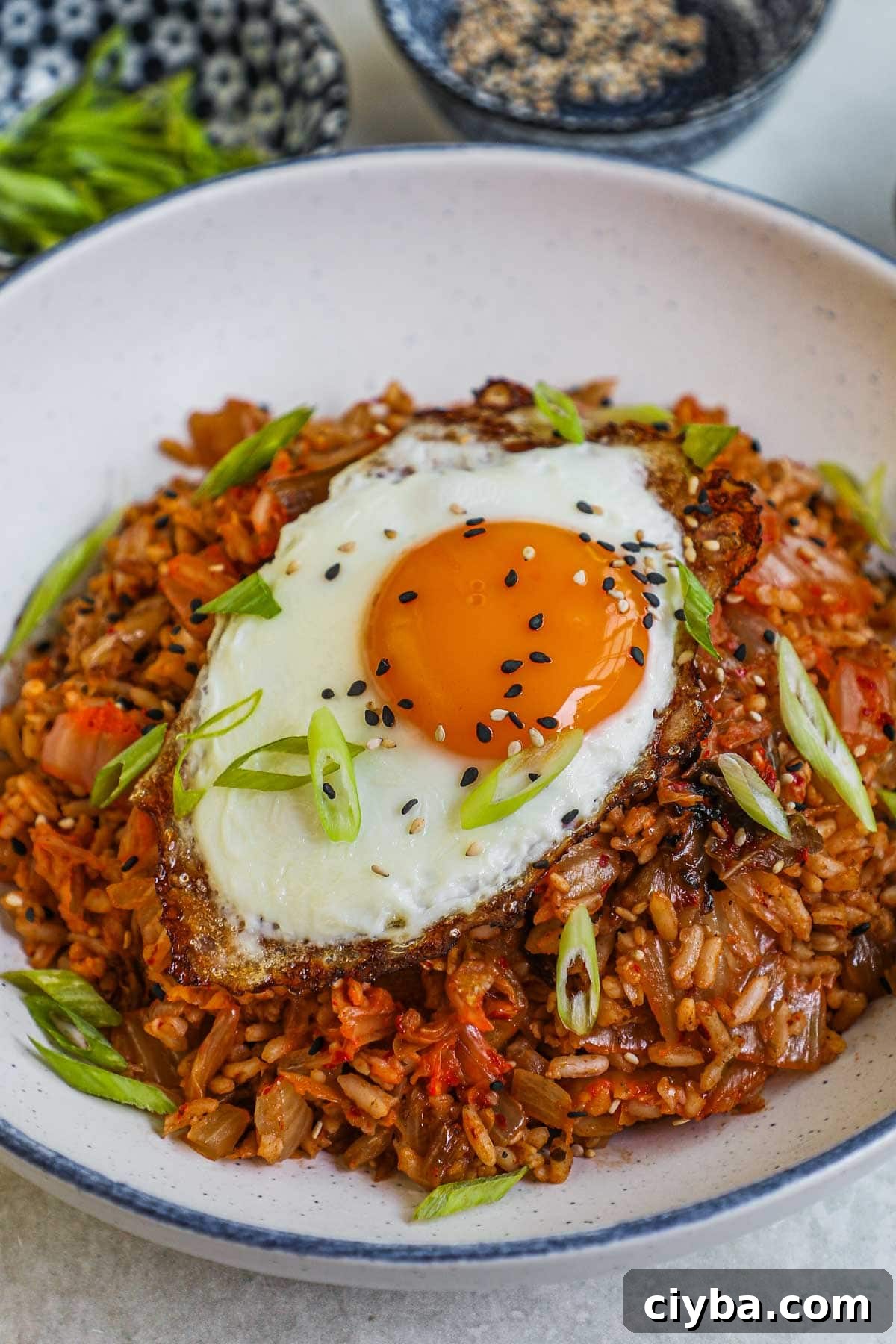 Closeup of kimchi fried rice with a fried egg, scallions, and sesame seeds.