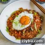 Easy kimchi fried rice in a bowl with a fried egg, sesame seeds, and scallions on top with chopsticks.