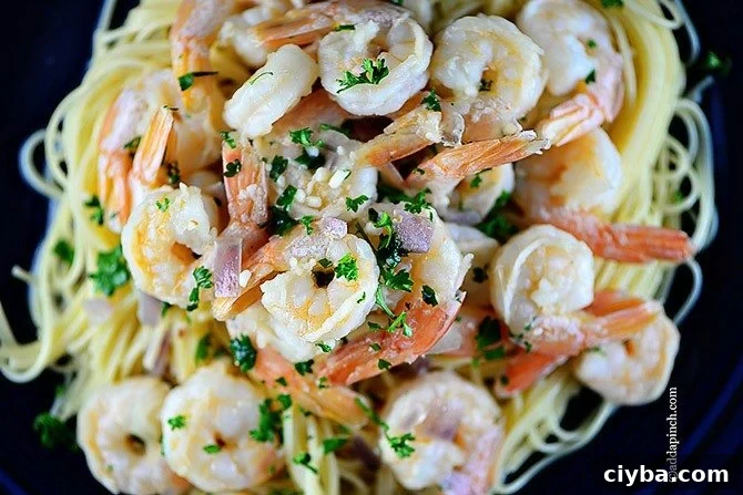 Overhead view of shrimp scampi on pasta, showing shrimp, garlic, red onion and fresh parsley // addapinch.com
