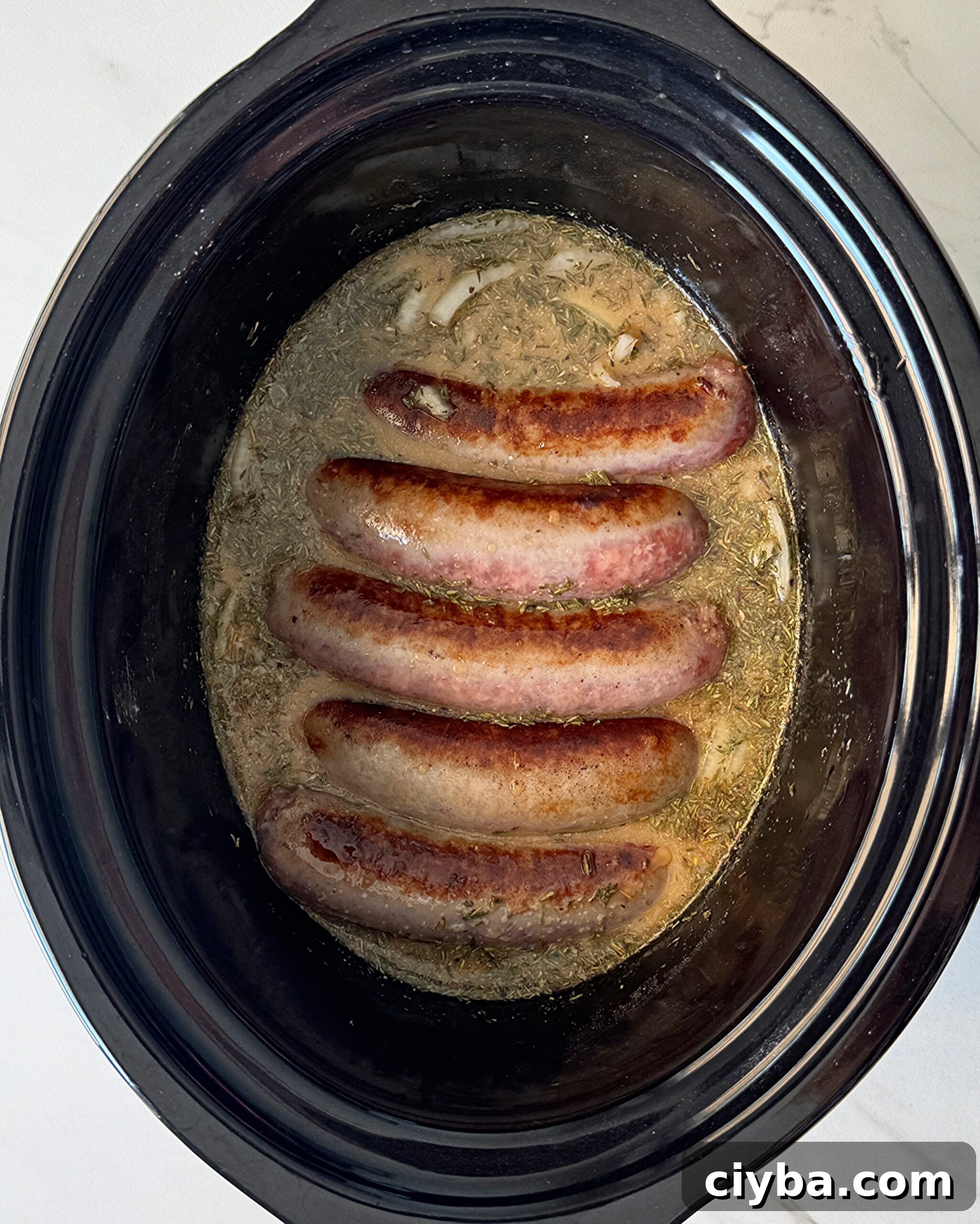 overhead shot of uncooked bangers & mash in a black slow cooker