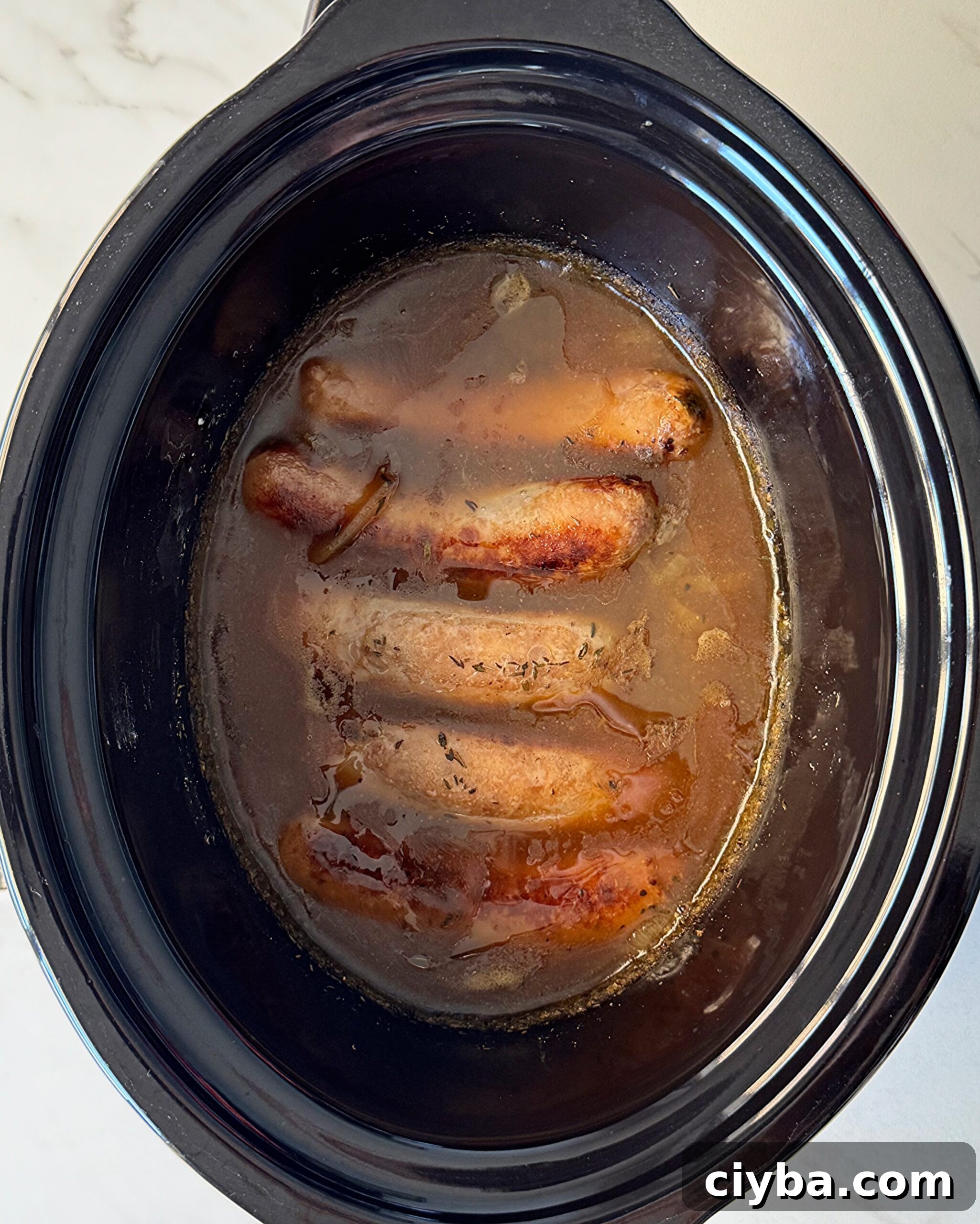 overhead shot of cooked bangers & mash in a black slow cooker