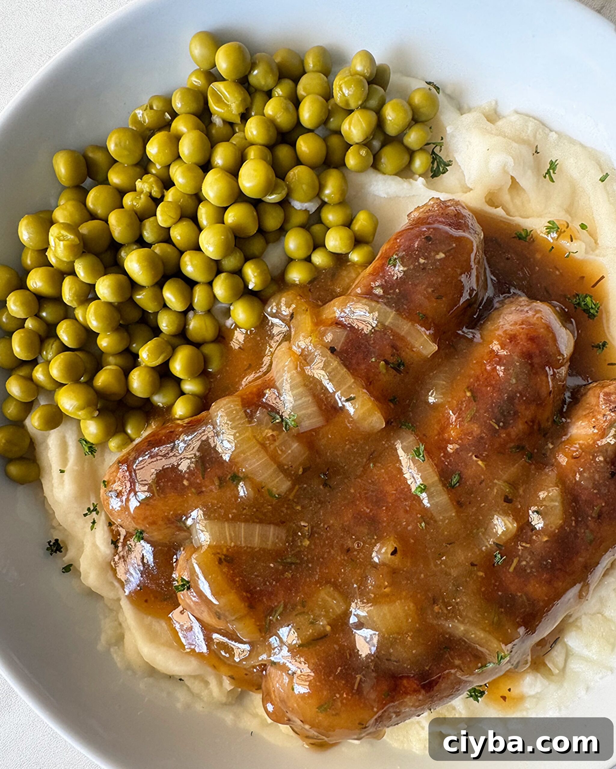 overhead shot of cooked bangers served over mashed potatoes with peas