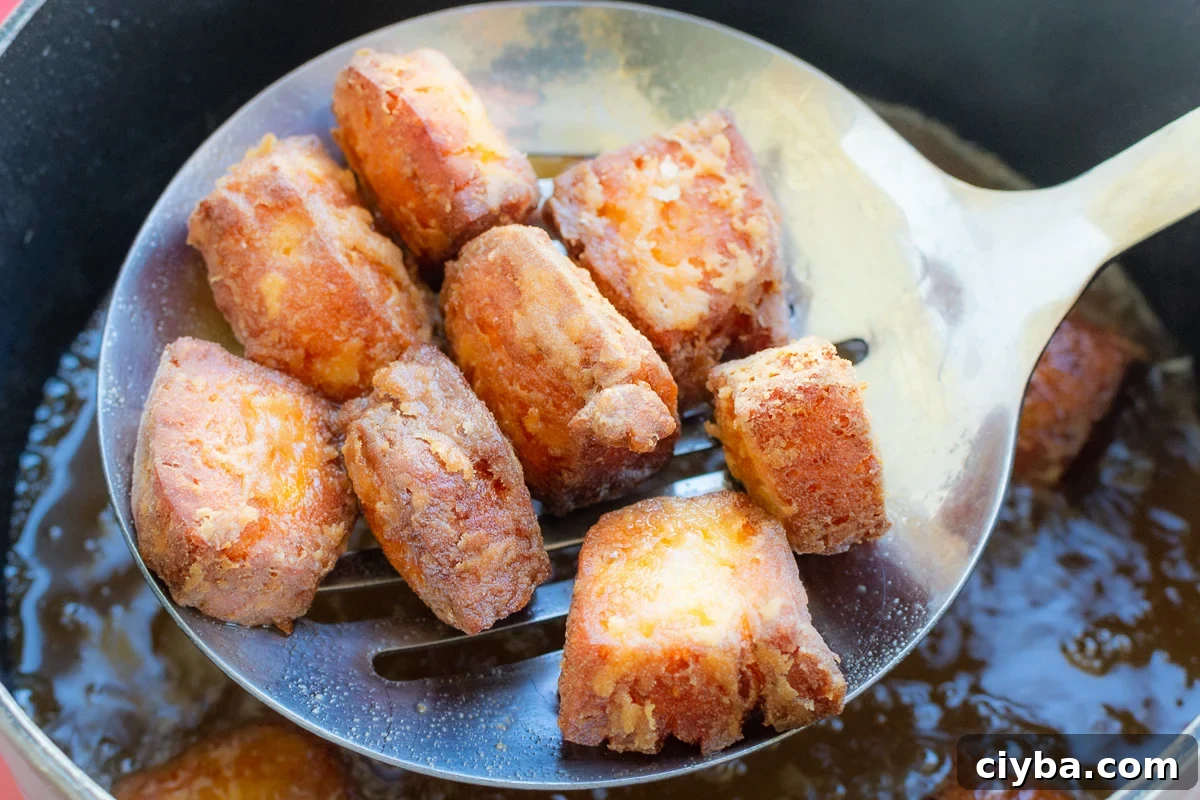 Crispy fried halloumi bites on a slotted spoon above a boiling hot pan of oil.