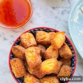 Overhead view of a small blue and red dish of crispy fried halloumi bites with small dishes of dipping sauces in the background.