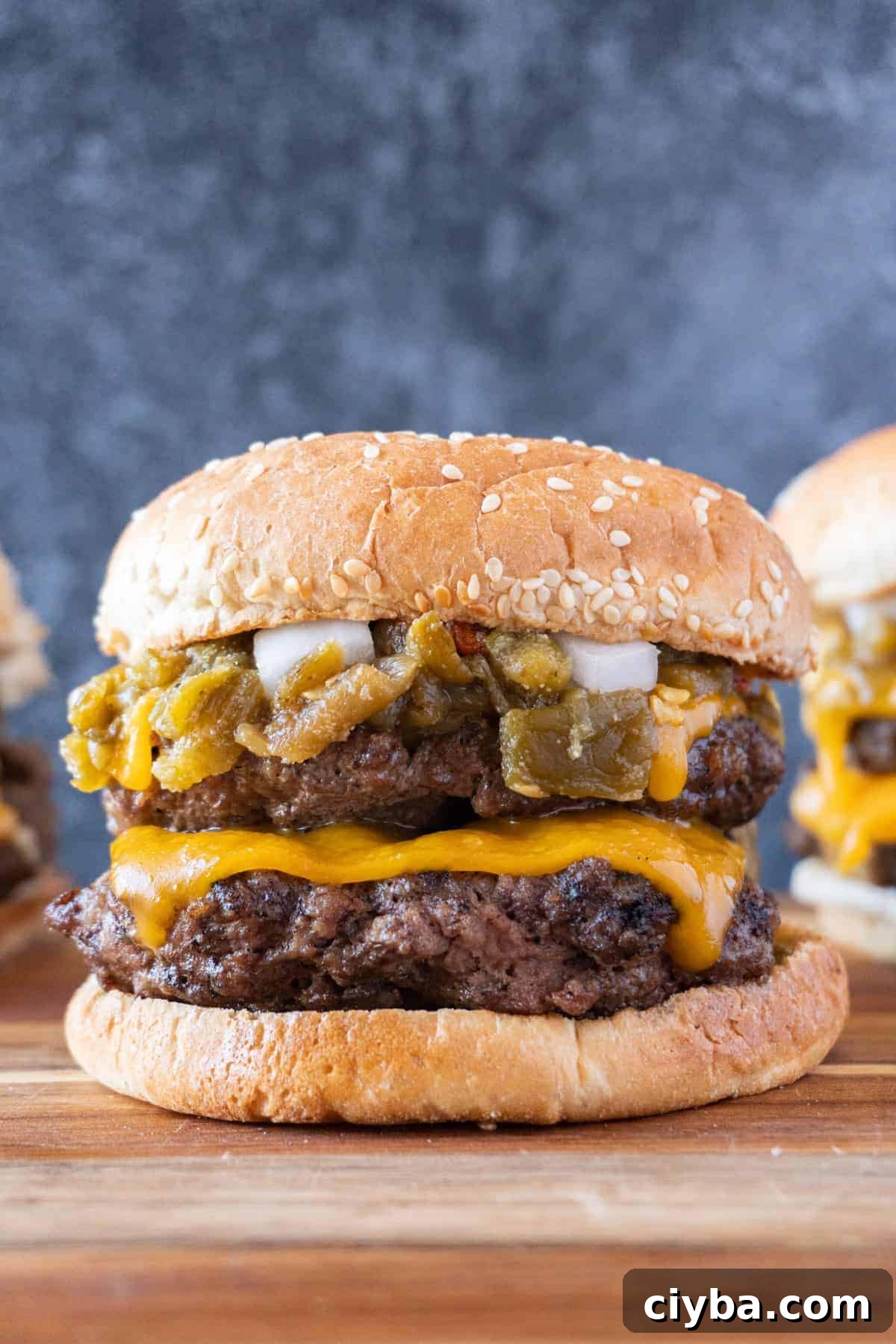 Double patty cheeseburger with green chile and a sesame bun on a wooden cutting board.