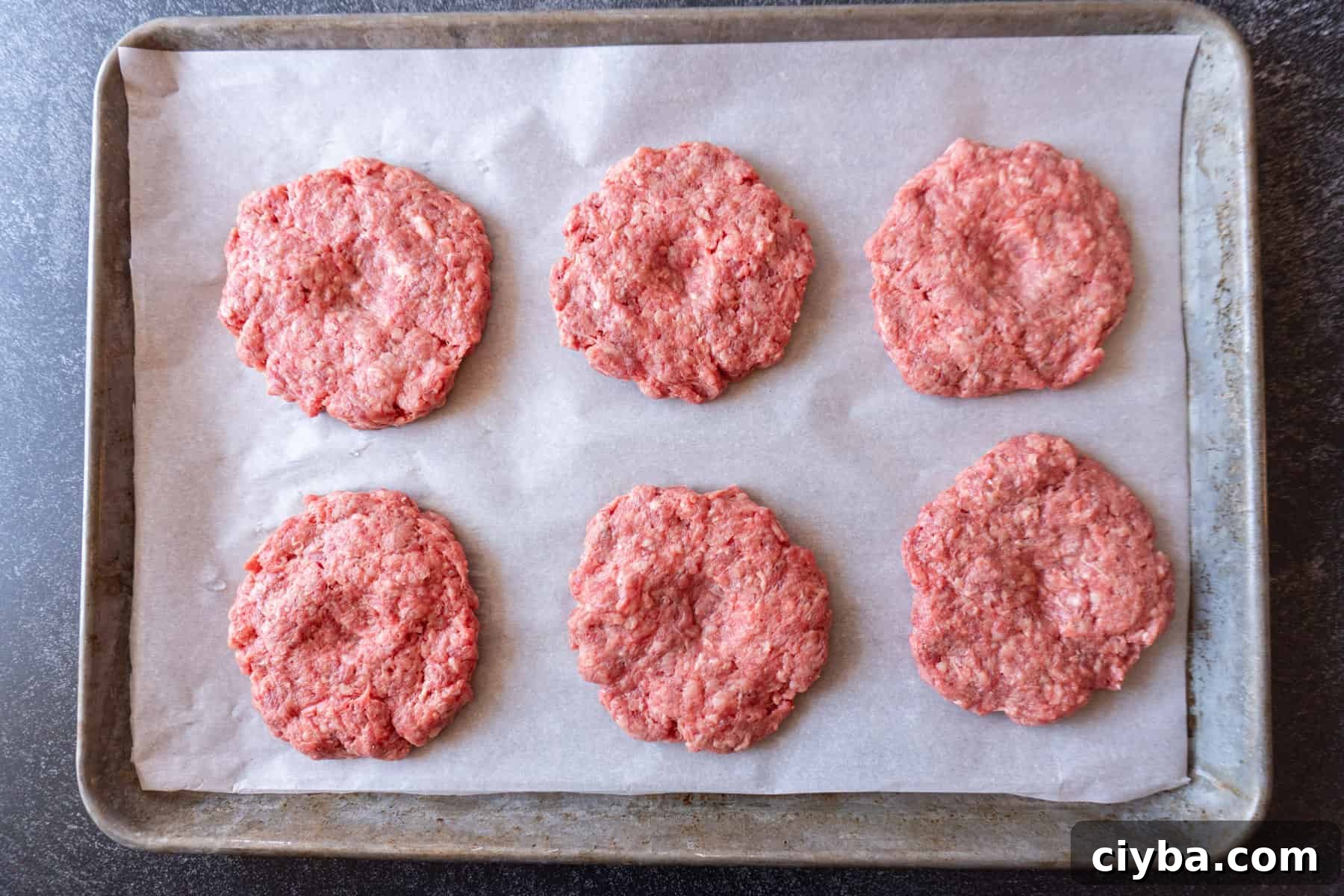 raw hamburger patties on a parchment-lined baking sheet.