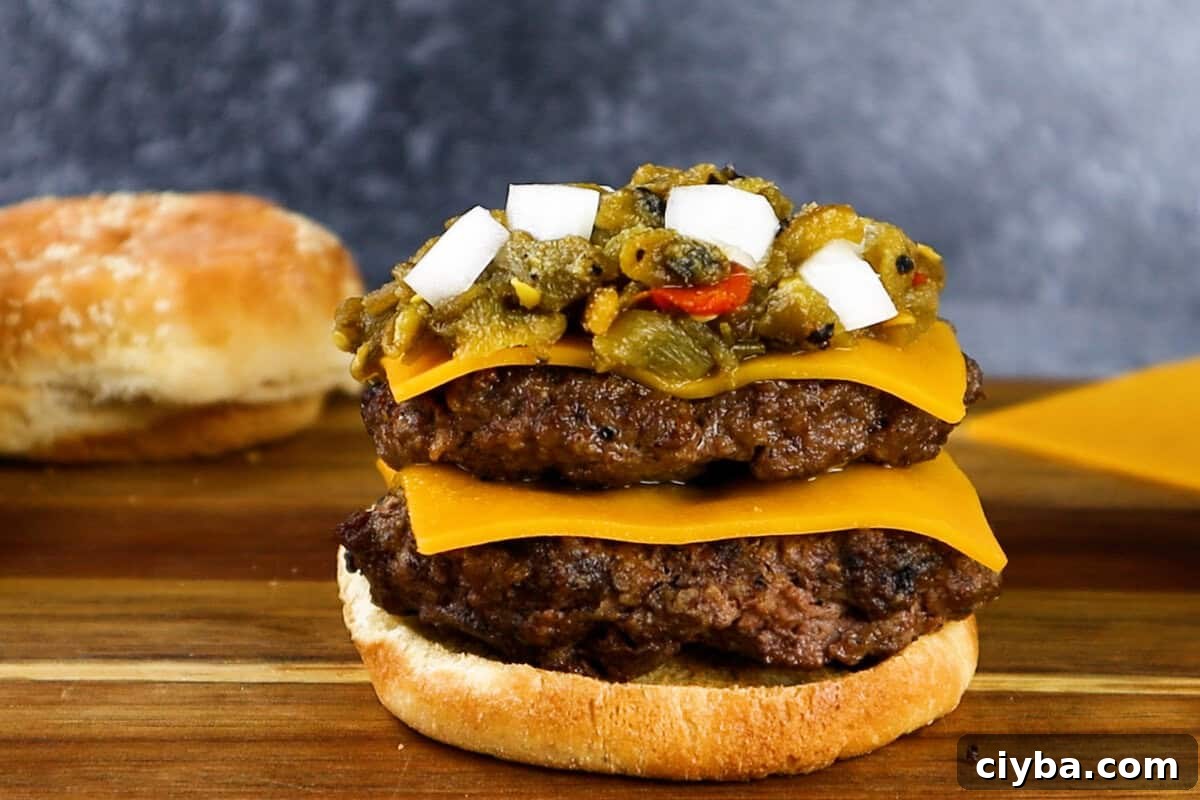 green chile cheeseburger being assembled- 2 patties with cheese. green chile and onion. 