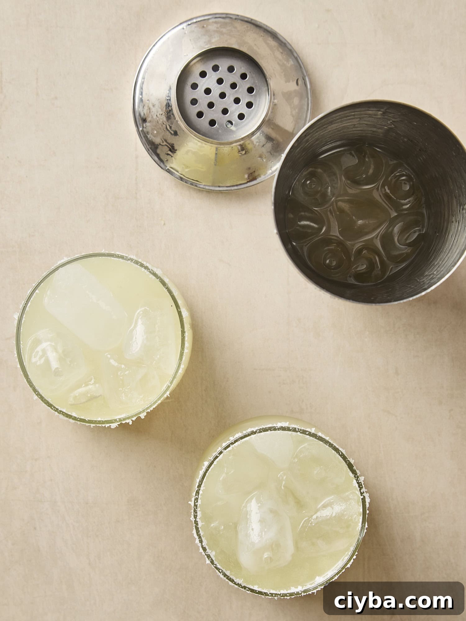 Classic Margarita Recipe: How to Make an Authentic Margarita 5 Two cocktail glasses filled with margarita with shaker open to the side.
