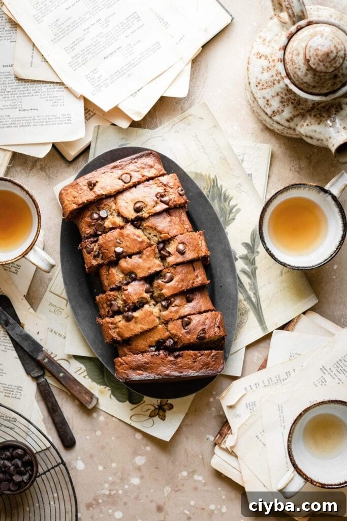 Sliced chocolate banana bread on plate with cups of tea.