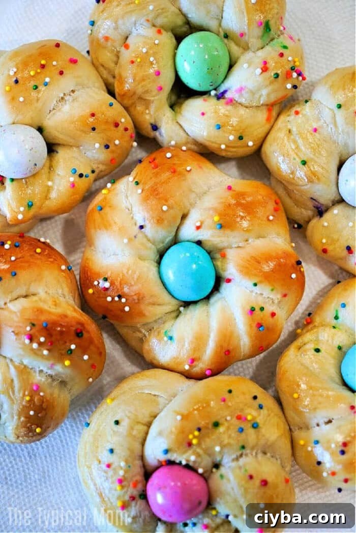 Sweet bread rolls twisted into rings, these delightful easter egg bread treats are topped with colorful eggs and rainbow sprinkles on a white background.