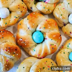Sweet bread rolls twisted into rings, these delightful easter egg bread treats are topped with colorful eggs and rainbow sprinkles on a white background.