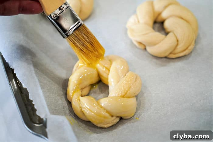 A pastry brush applies egg wash to an Easter egg bread braided dough ring on a parchment-lined baking sheet.