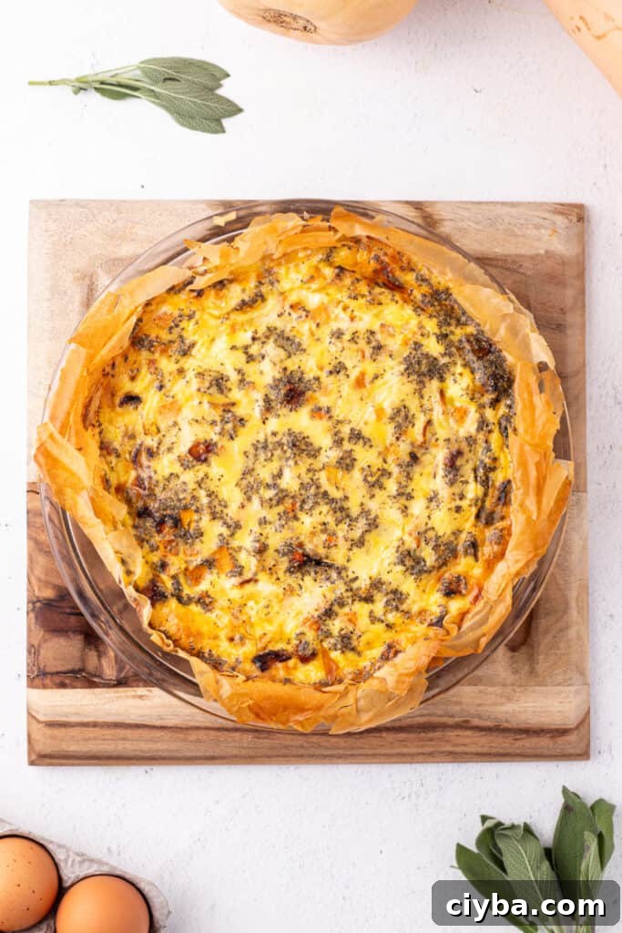 Baked roasted squash quiche in a phyllo crust, golden brown on top and resting on a wooden board with fresh sage nearby.
