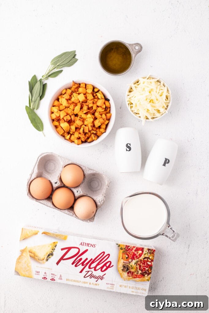 Overhead view of ingredients for roasted squash quiche including roasted butternut squash, fresh sage, olive oil, eggs, phyllo dough, shredded Gruyère cheese, half and half, and salt and pepper shakers.