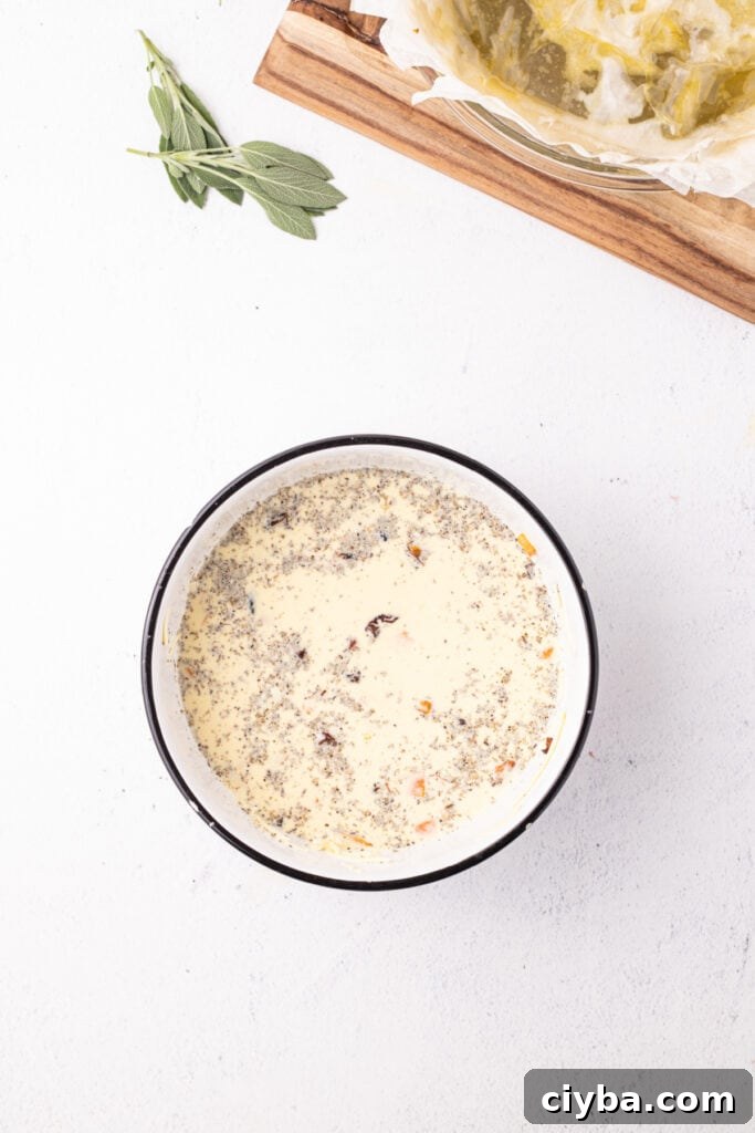 Bowl with quiche filling mixture of eggs, cream, squash, cheese, and sage, seasoned and ready to pour into the crust.