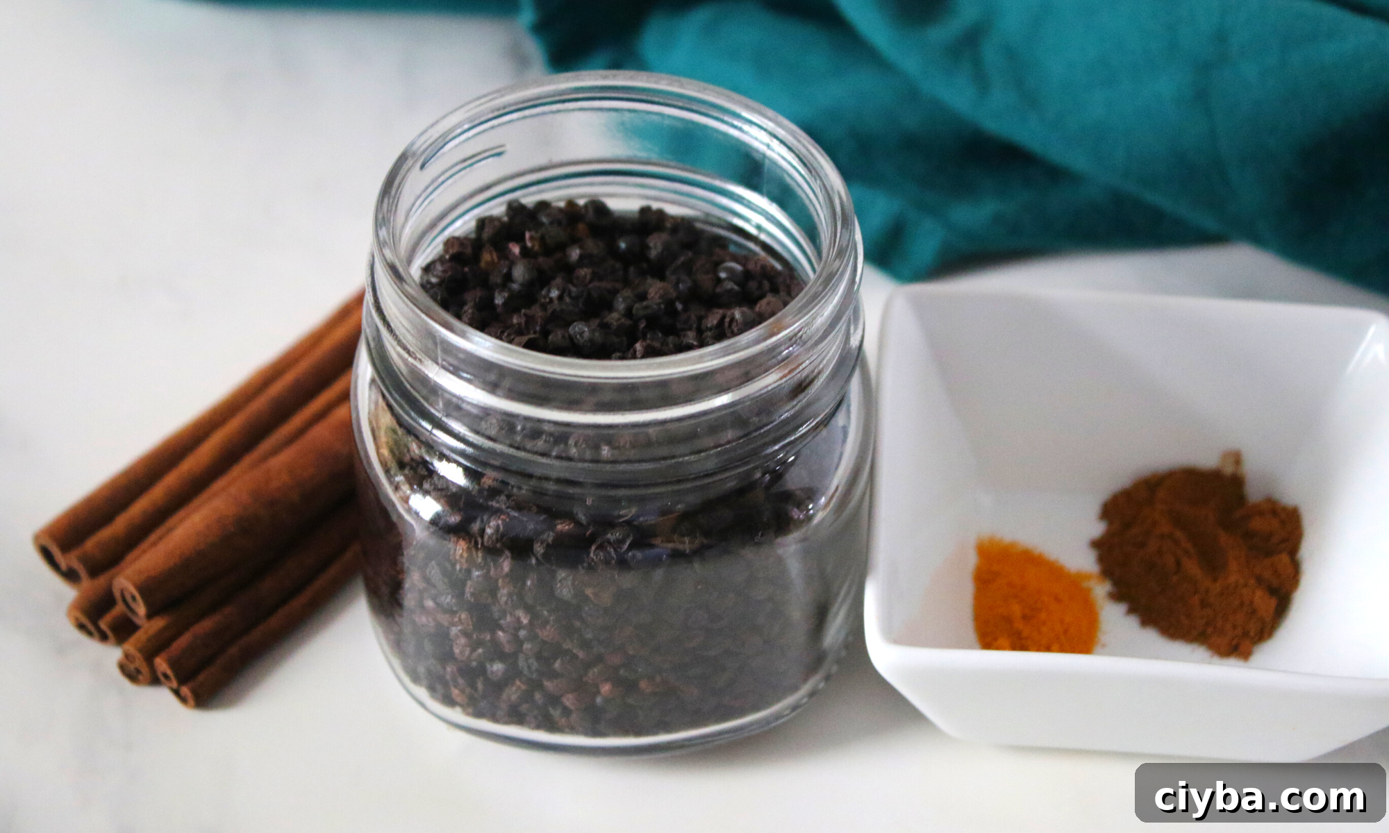 A glass jar of dried elderberries next to a cup of spices. 