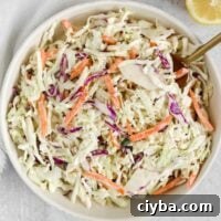 Creamy coleslaw in a serving bowl with a gold spoon.