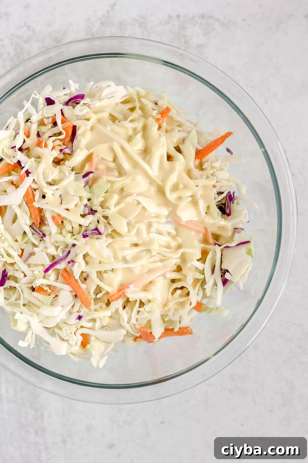 Creamy Whole30 and Paleo Coleslaw Recipe for BBQs and Meals 5 Dressing poured on coleslaw mix in a mixing bowl.