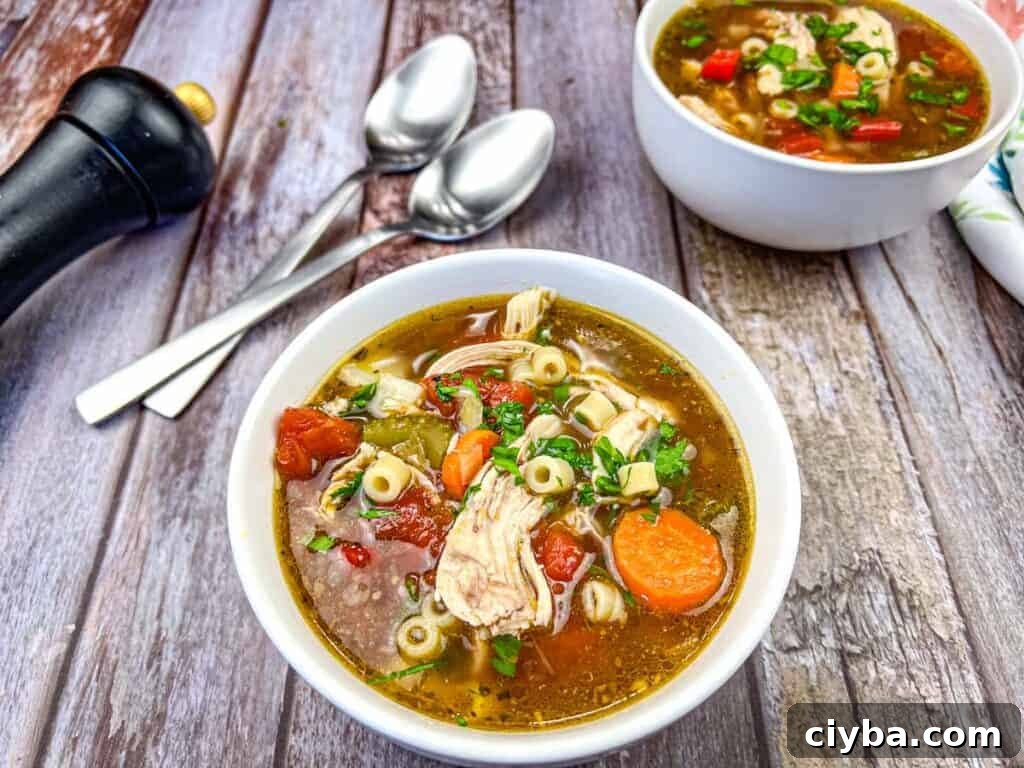 Two bowls of Copycat Carrabba's Mama Mandola's Sicilian Chicken Soup, accompanied by two spoons, a black pepper grinder, and a napkin.