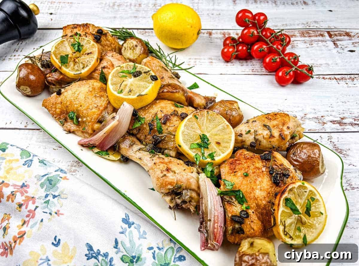 A platter of sheet pan lemon-rosemary chicken with lemon slices, herbs, and garnished with cherry tomatoes.