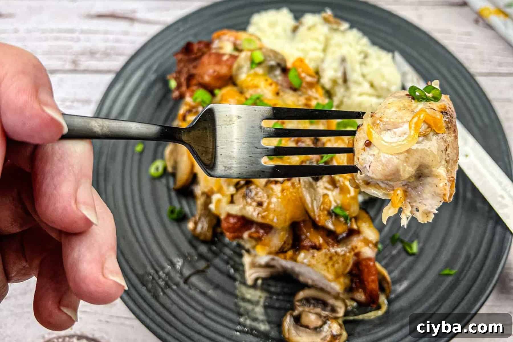 Close-up of a hand holding a fork with a bite of copycat Alice spring chicken.