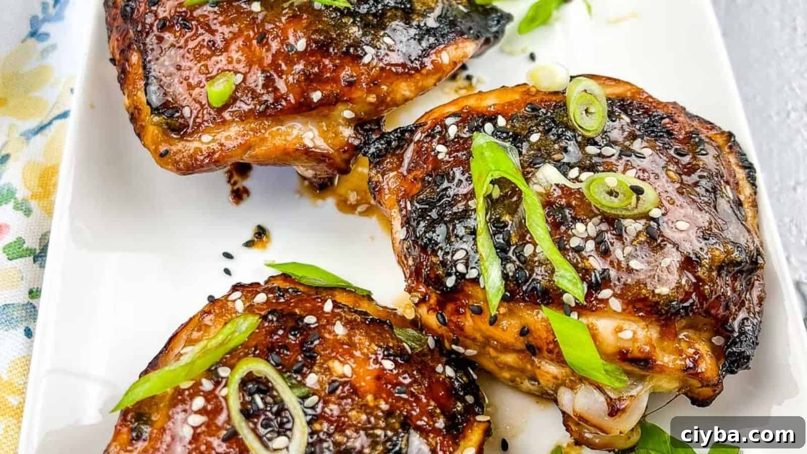 Three pieces of Air Fryer Honey Garlic Chicken garnished with sesame seeds and chopped green onions on a white rectangular plate.