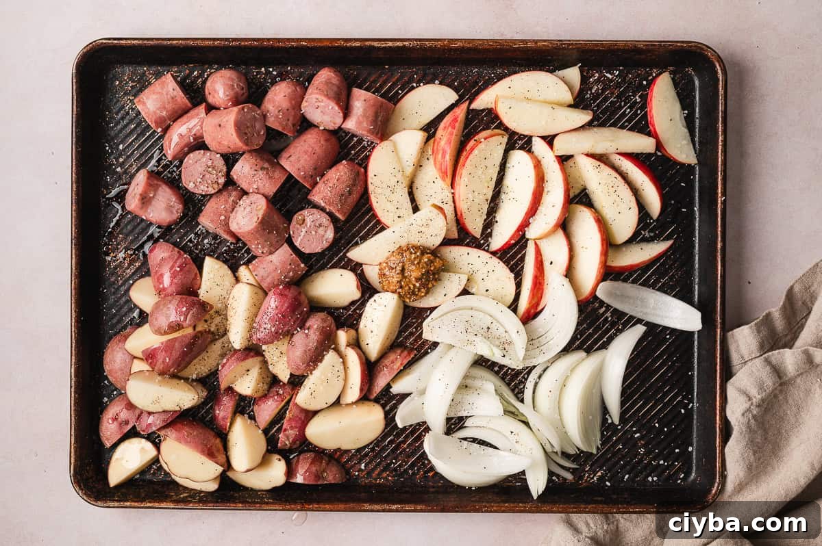 Chicken sausage, potatoes, apples, and onion on a baking sheet