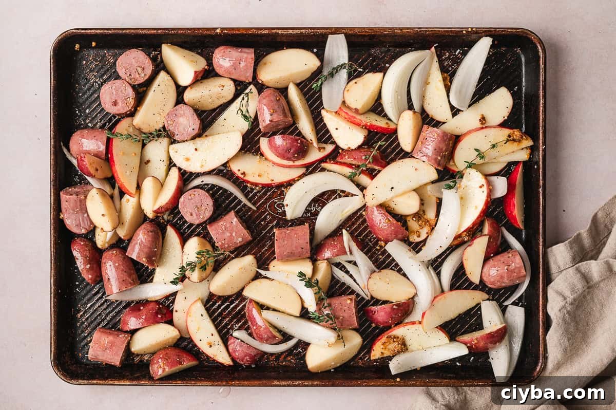 Chicken sausage, apples, onion, and potatoes on a baking sheet