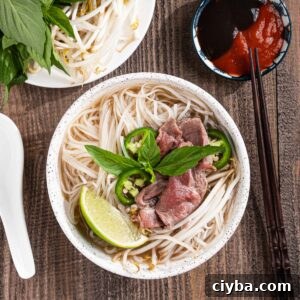 Bowl of pho tai with lime wedges, herbs, hoisin sauce, and sriracha.