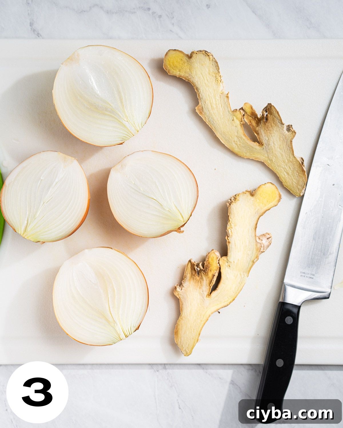 Cutting board and knife with onions and ginger sliced in half.