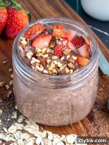 Nutella overnight oats in a mason jar topped with strawberries, Nutella, and hazelnuts.