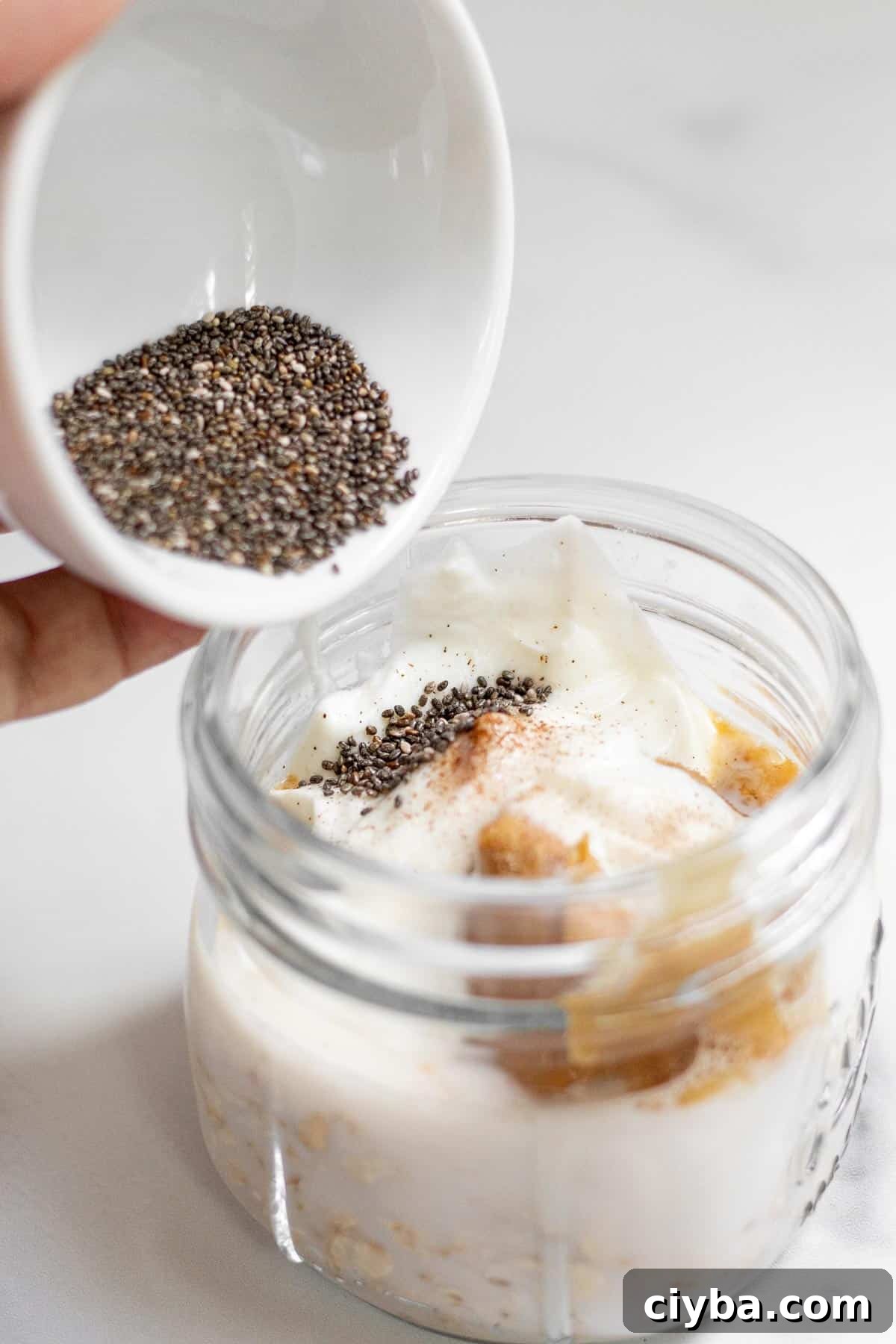 Pouring chia seeds into a 12 oz jar that contains the other ingredients for overnight oats with protein powder.