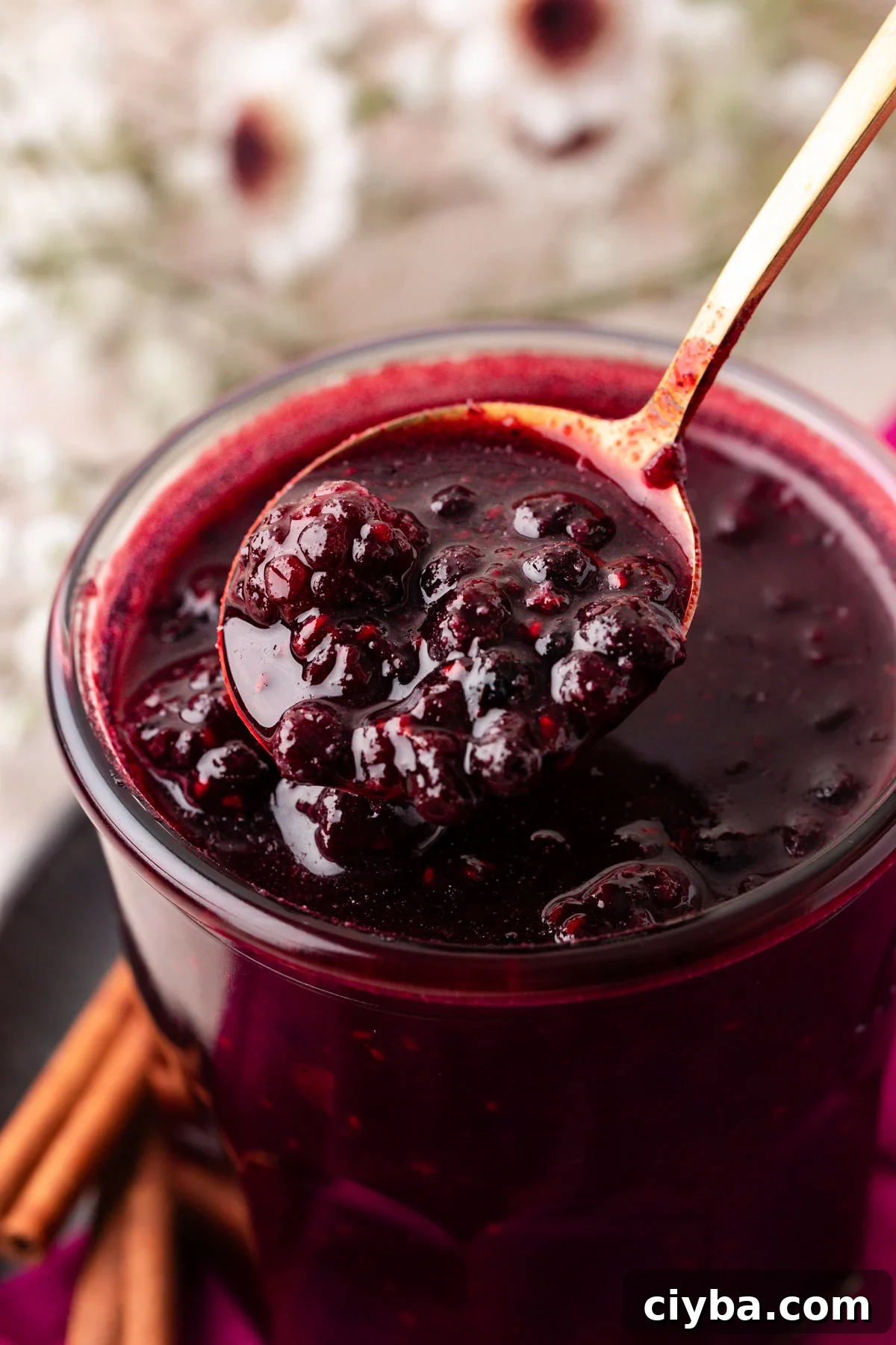 Close up of a jar of berry compote with a spoon lifting some out.