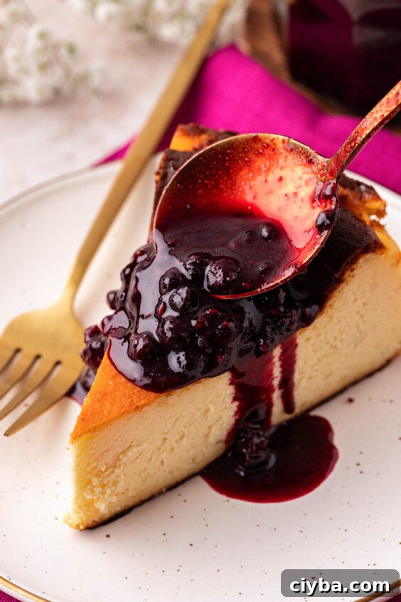 Berry compote being spooned over a slice of cheesecake.