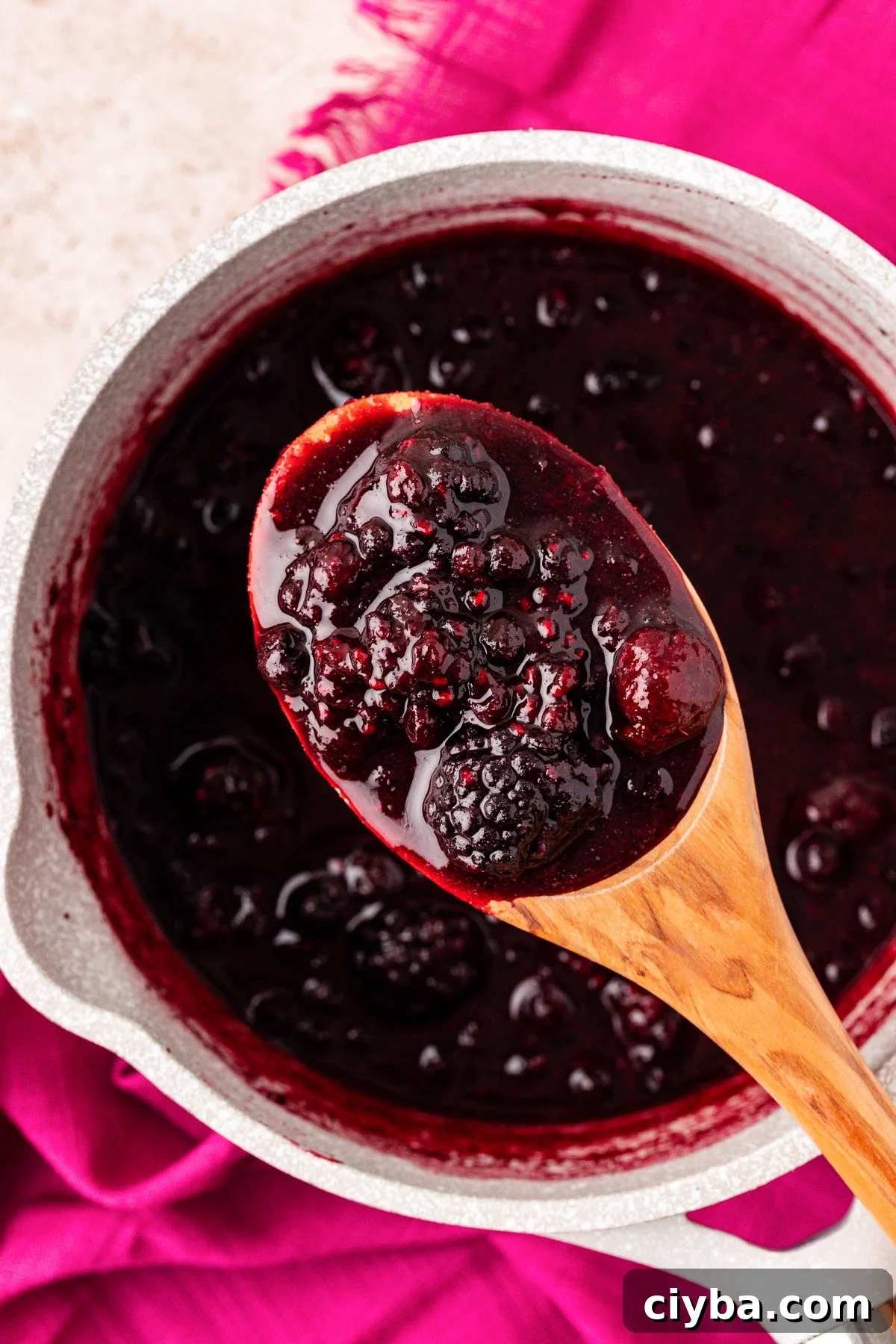 A serving spoon with mixed berry compote over a pot.