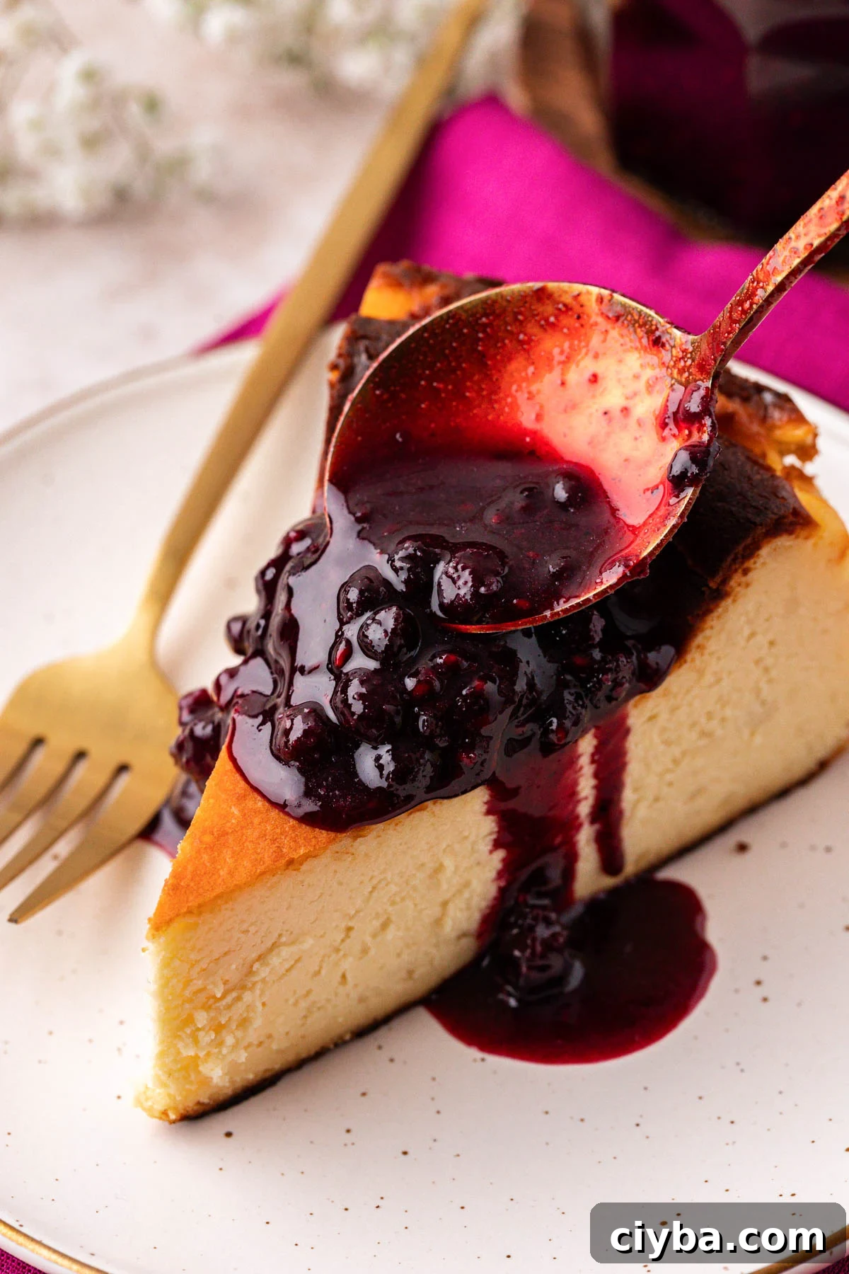 Berry compote being spooned over a slice of cheesecake.