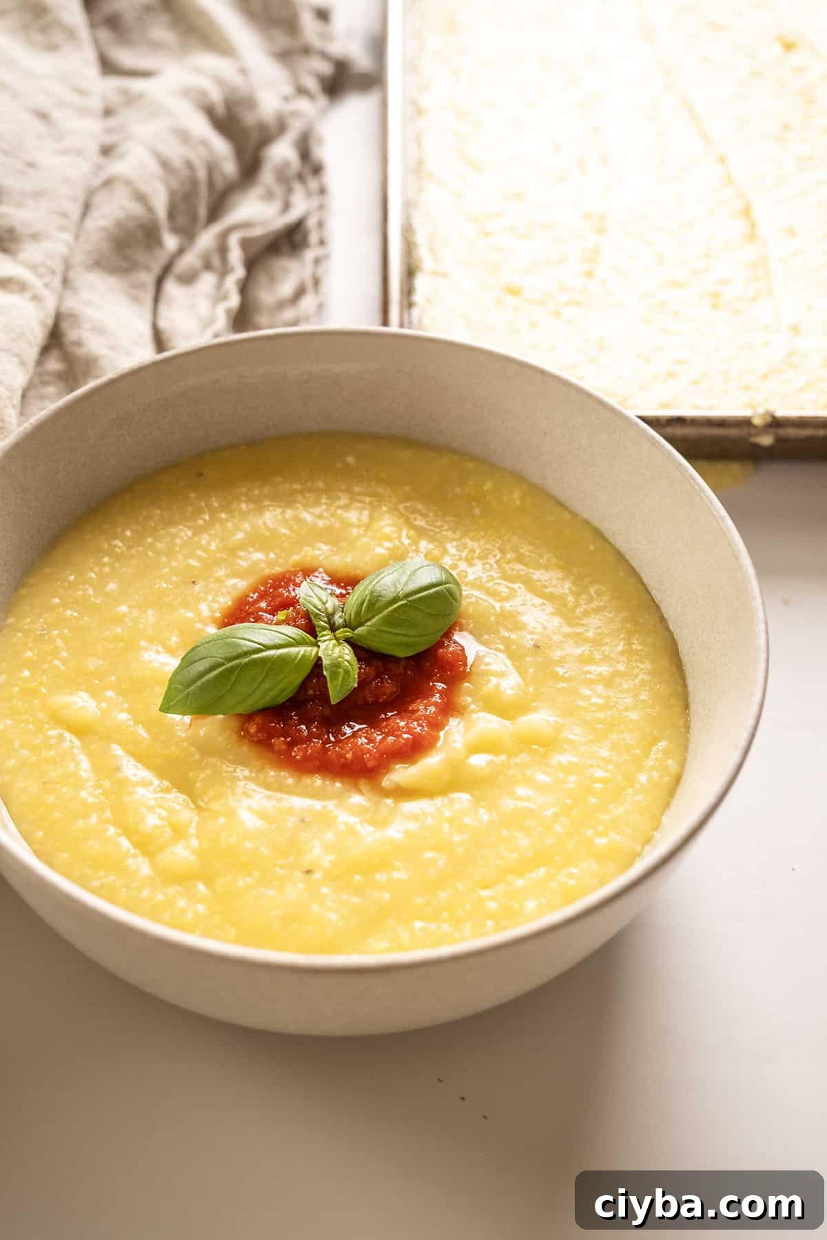 Creamy polenta in a bowl topped with marinara and basil.