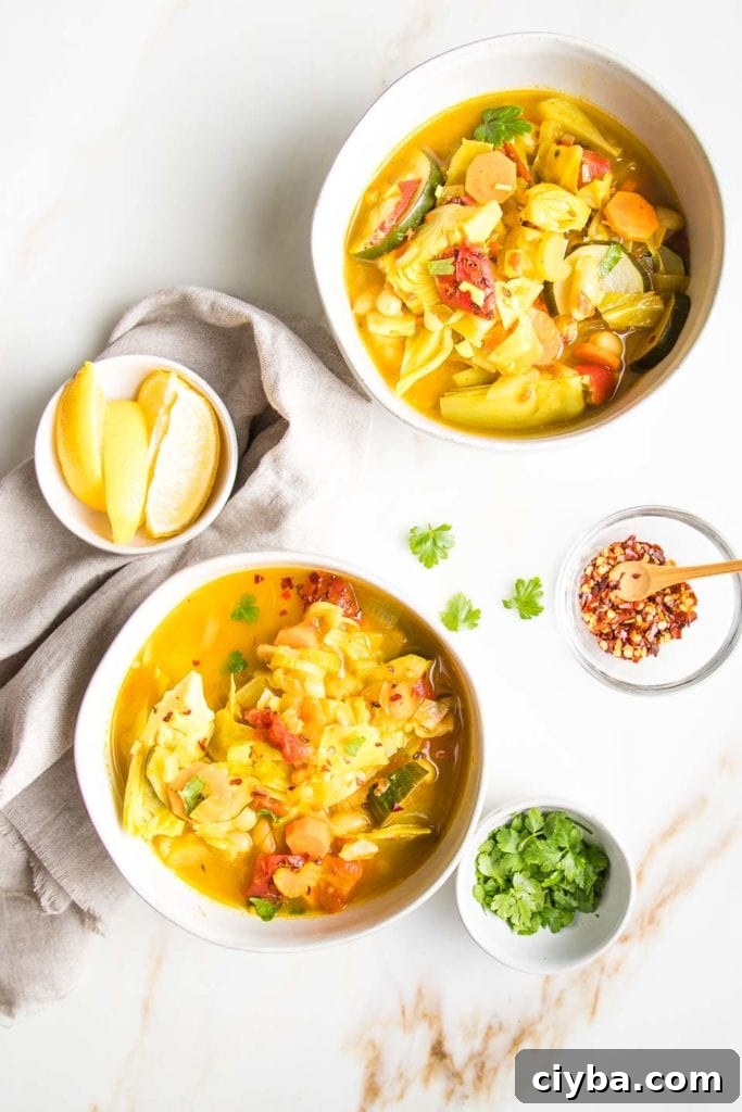 Homemade Garden Vegetable Soup Recipe for Comforting Meals 7 Two bowls of brothy, chunky vegetable soup with garnishes: lemon wedges, crushed red pepper, and chopped parsley.