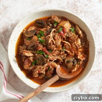 A large bowl of slow cooker chicken cacciatore with a wooden spoon in it. A red and white striped napkin is on the left.