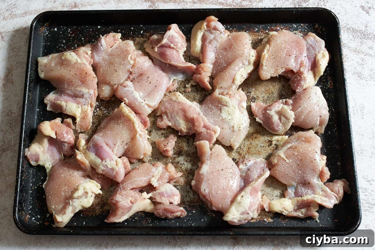 Raw chicken thighs seasoned with salt and pepper on a sheet pan.