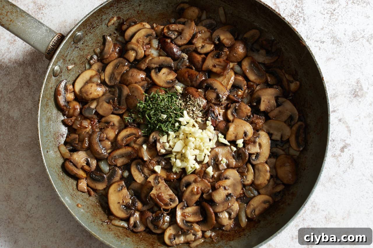 Cooked mushrooms in a skillet with diced garlic and chopped rosemary added.