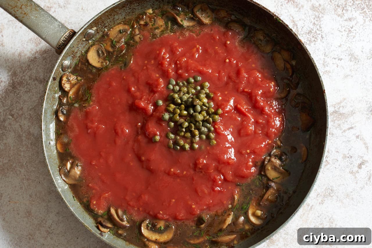 Tomatos and capers being added to a skillet of mushrooms and broth.