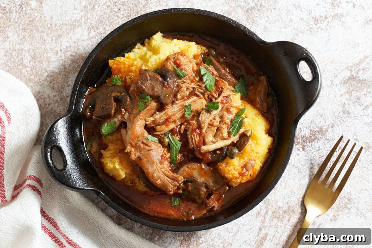 A cast iron serving dish of slow cooker chicken cacciatore over polenta. A gold forks is on the right, a red and white striped towel is on the left.