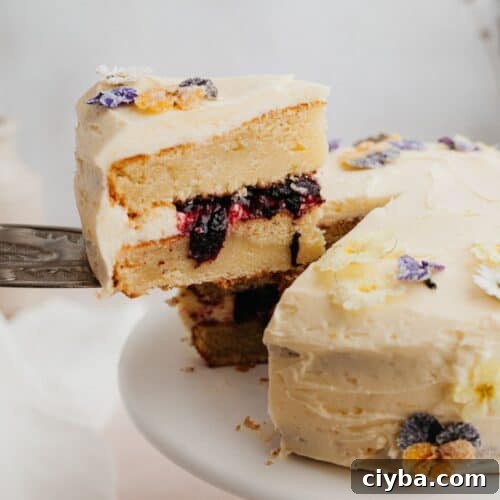 A yellow cake with a blueberry filling, a silver cake server is lifting one slice out.