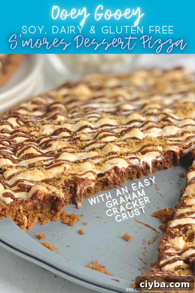 S'mores Dessert Pizza Recipe: Gooey Campfire-Inspired Treat 2 A pizza pan layered with a graham cracker crust, melted chocolate, golden brown mini marshmallows, then drizzled with chocolate and topped with graham cracker crumbs. A large slice is removed from the pizza.